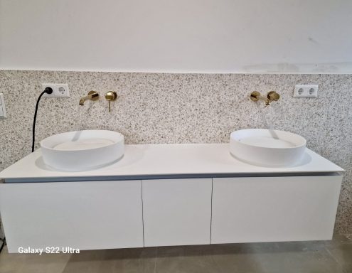 Zwei runde Waschbecken auf einem weißen Unterschrank mit goldenen Wasserhähnen.