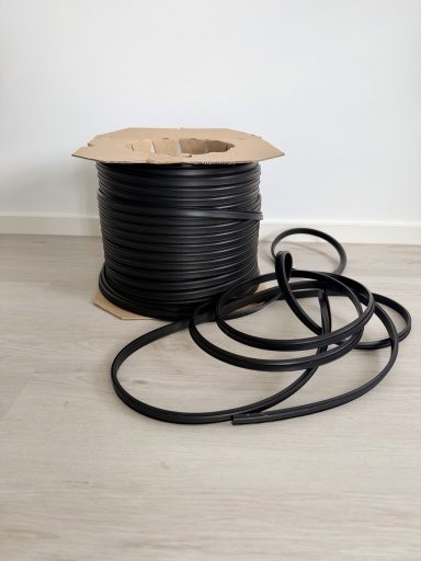 Gummidichtung Schwarzes Kabel auf einer Rolle, mit losem Ende auf dem Boden liegend.