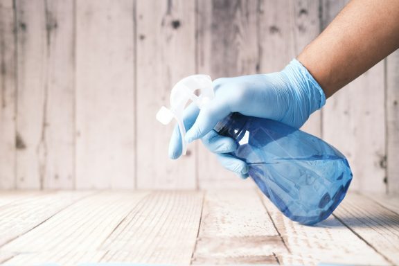 Hand mit blauer Gummihand schüttet eine Reinigungsflasche aus.