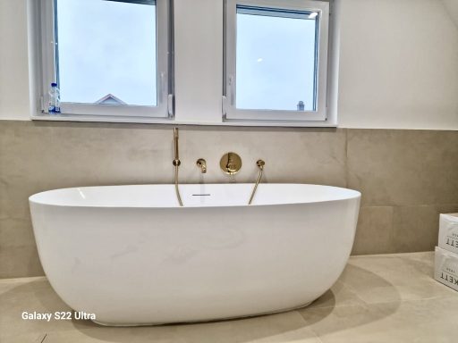 Moderne, freistehende Badewanne vor einem Fenster mit hellem, neutralem Wanddesign.
