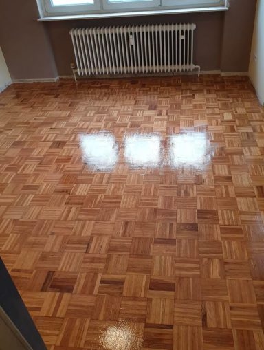 Holzboden aus Parkett mit glänzender Oberfläche und sichtbaren Fensterreflexionen.